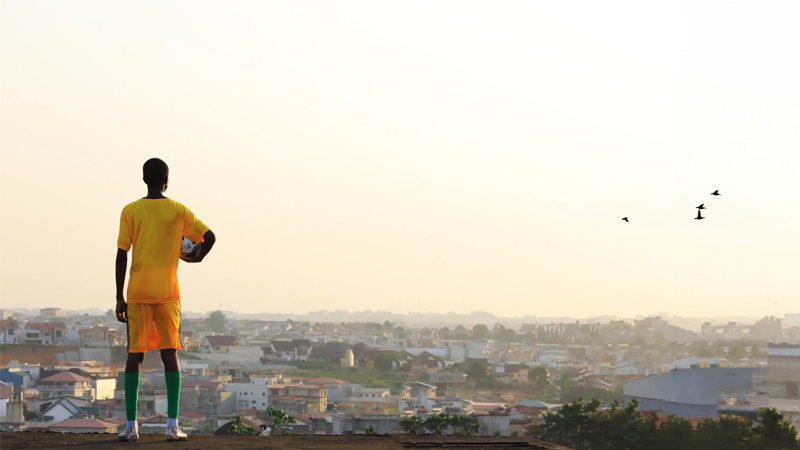 A football player holds the ball and looks at the morning city from the roof, TotalEnergies CAF AFCON 2023